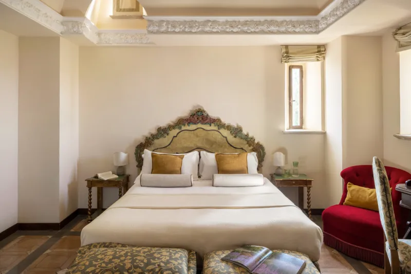 Tower Suite with double bed, ornate headboard and red armchair in refined Tuscan hospitality style - La Collegiata, BZAR hotels in Tuscany